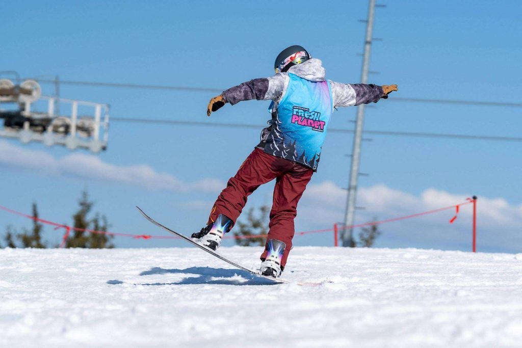 Skier in a blue jacket lands a jump on a snowy slope, wearing a helmet and red pants.