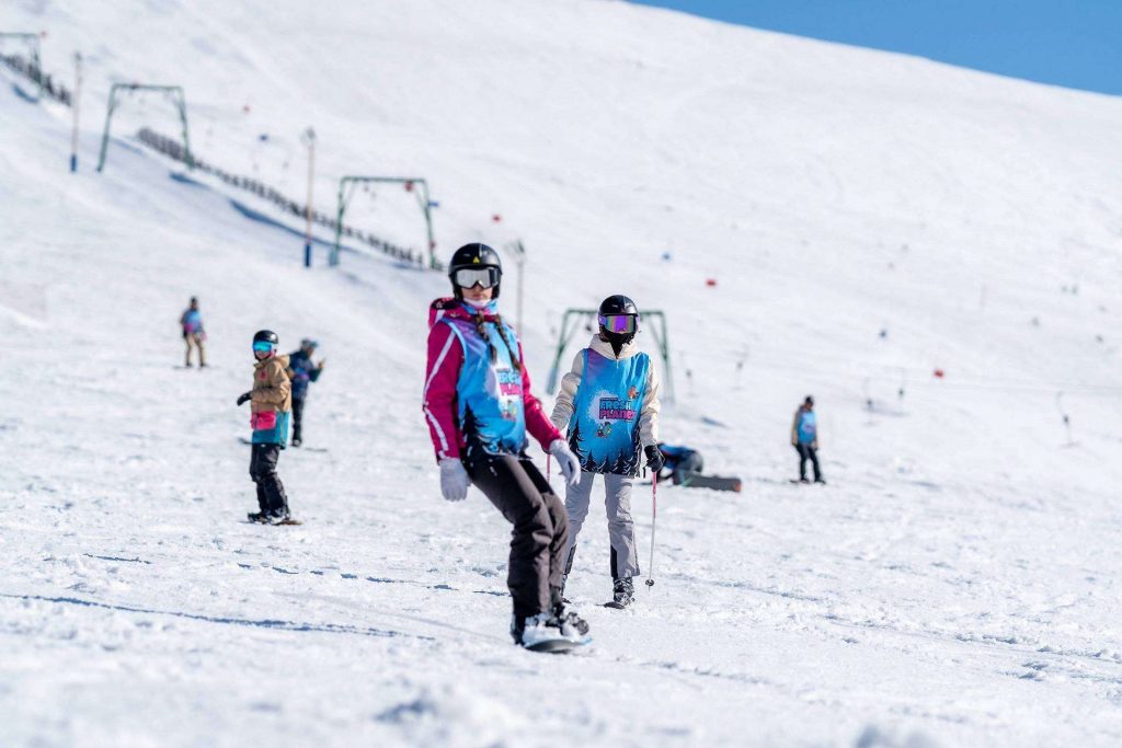 Kids in colorful ski outfits skiing on a snowy slope under a clear blue sky.**
