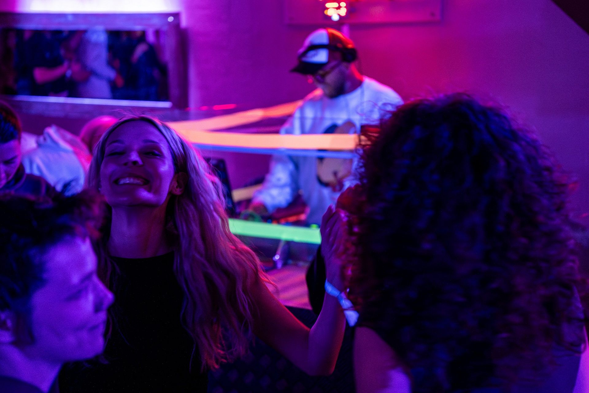 ADR05372-Enhanced-NR snow vars | Fresh Planet | Fresh Planet Woman smiling at a crowded club with a DJ in the background under purple and pink lights.