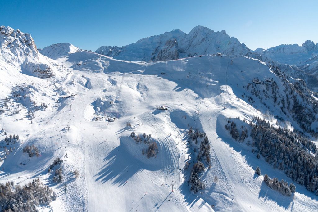 Snow-covered alpine slopes with chairlifts and evergreen trees under a clear blue sky.