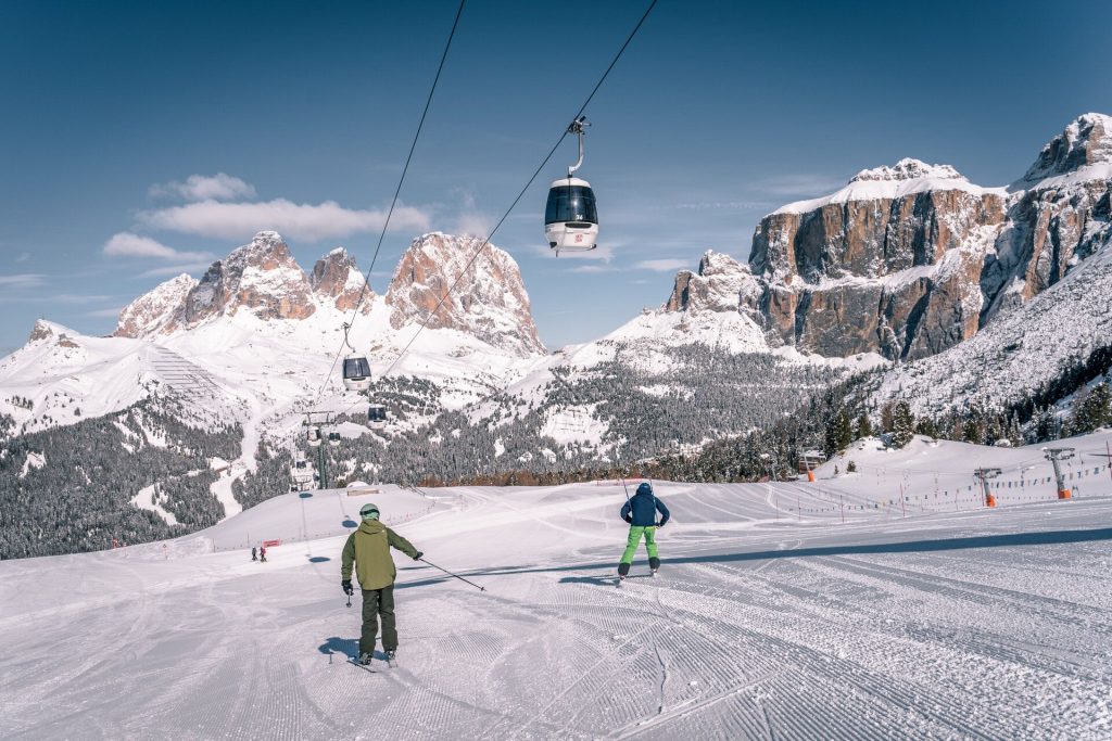 Gondola cable car gliding above a snowy alpine ski slope with rugged mountain peaks in the background.