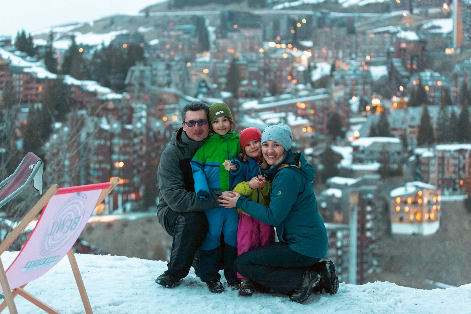 FJ7B6918 snow avoriaz | Fresh Planet | Fresh Planet Family of four in winter jackets posing together on snow with a town in the snowy hillside behind them.