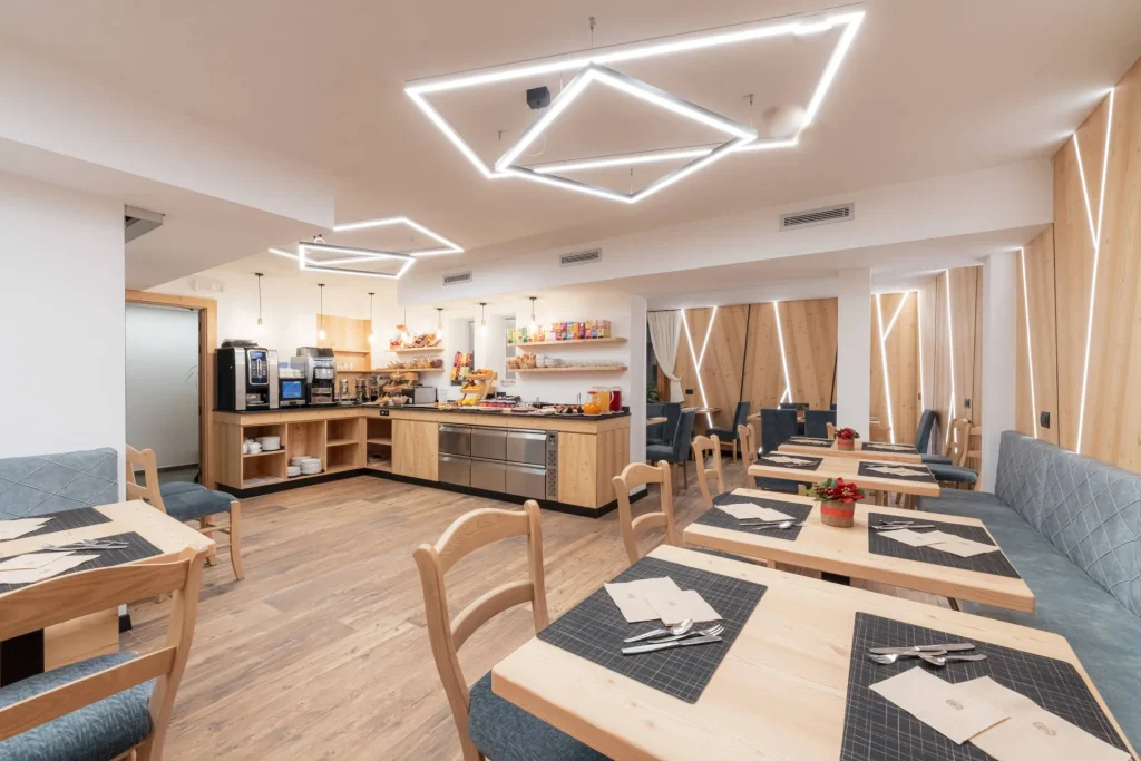 Bright modern cafe interior with wooden tables, blue upholstered seating, and a self-serve counter stocked with snacks and coffee machines.